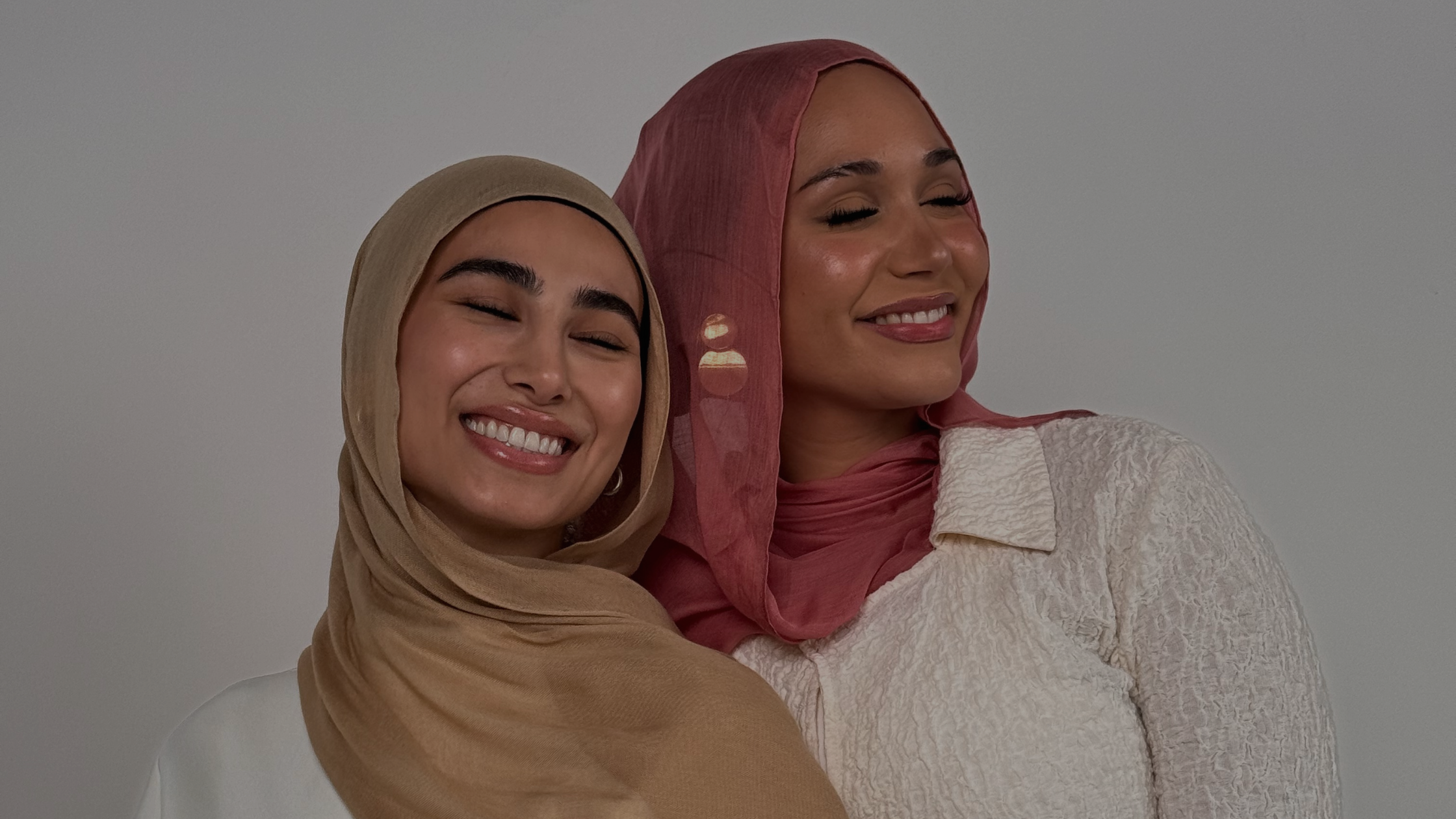 Two girls smiling next to each other wearing headscarves.