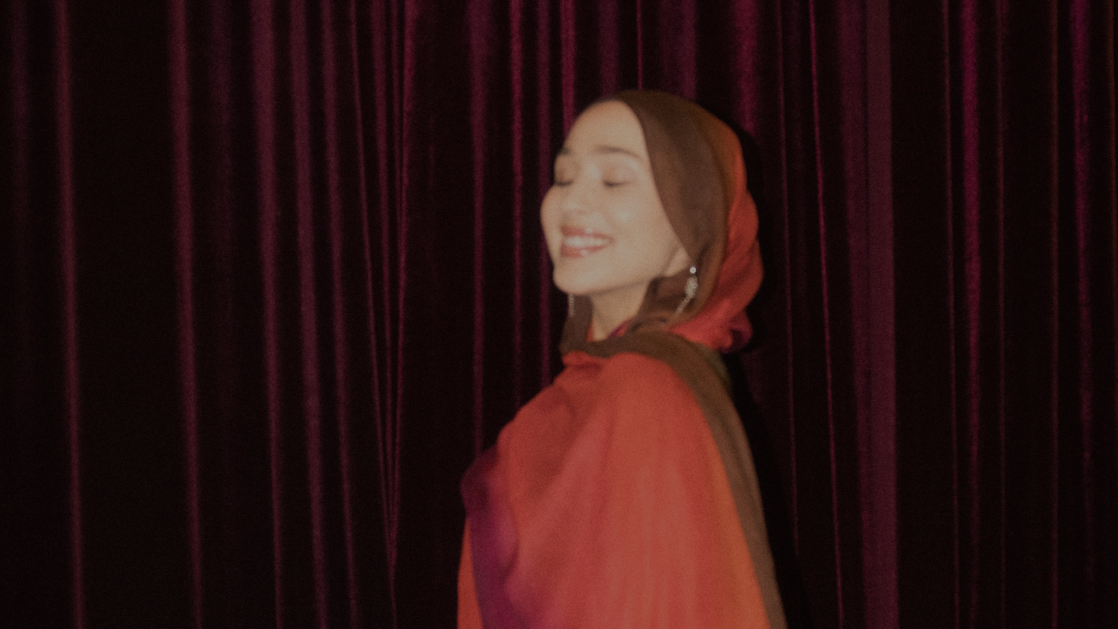 A Muslim smiling in front of a red backdrop.