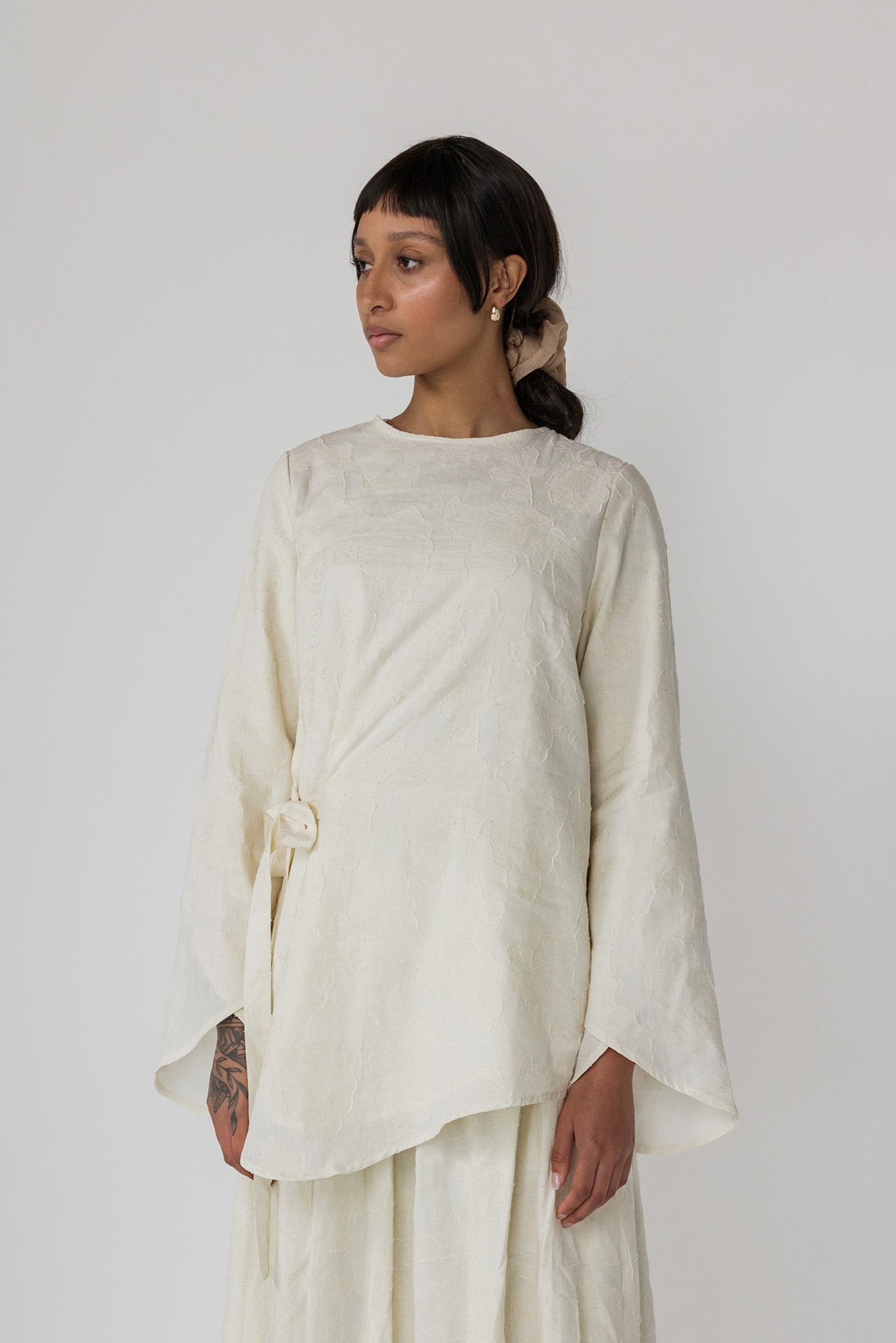 Cream-colored textured top with a gentle drape and feminine front tie