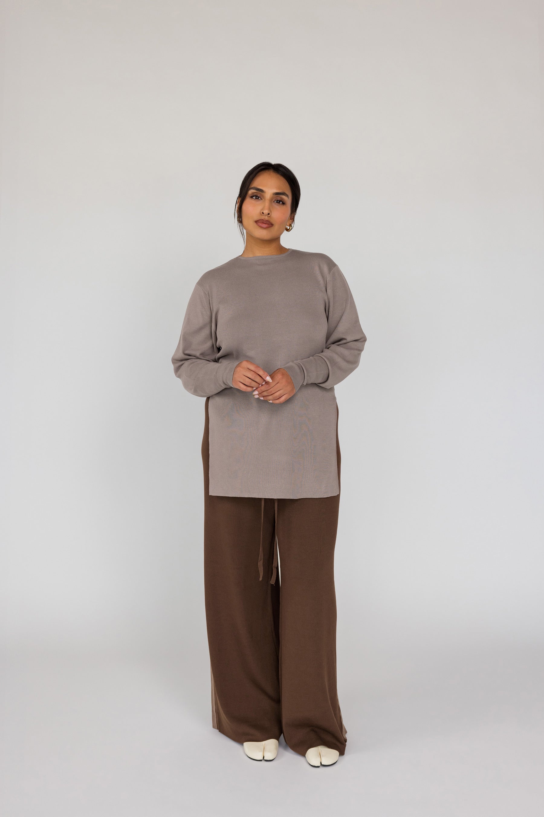 Woman wearing a beige top and brown pants on a white background