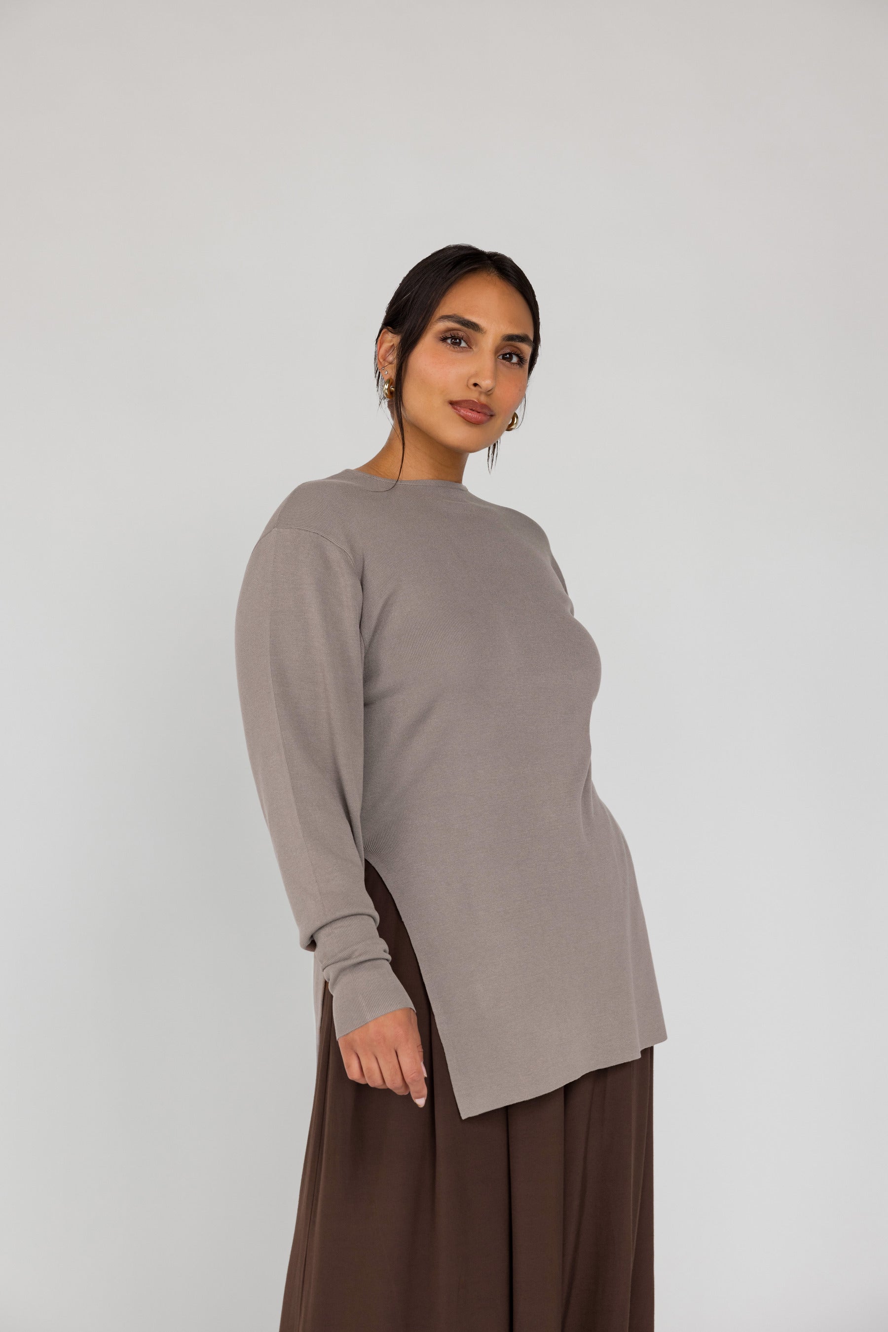 Woman wearing a long-sleeve beige top and brown pants on a white background