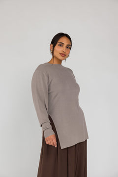Woman wearing a long-sleeve beige top and brown pants on a white background