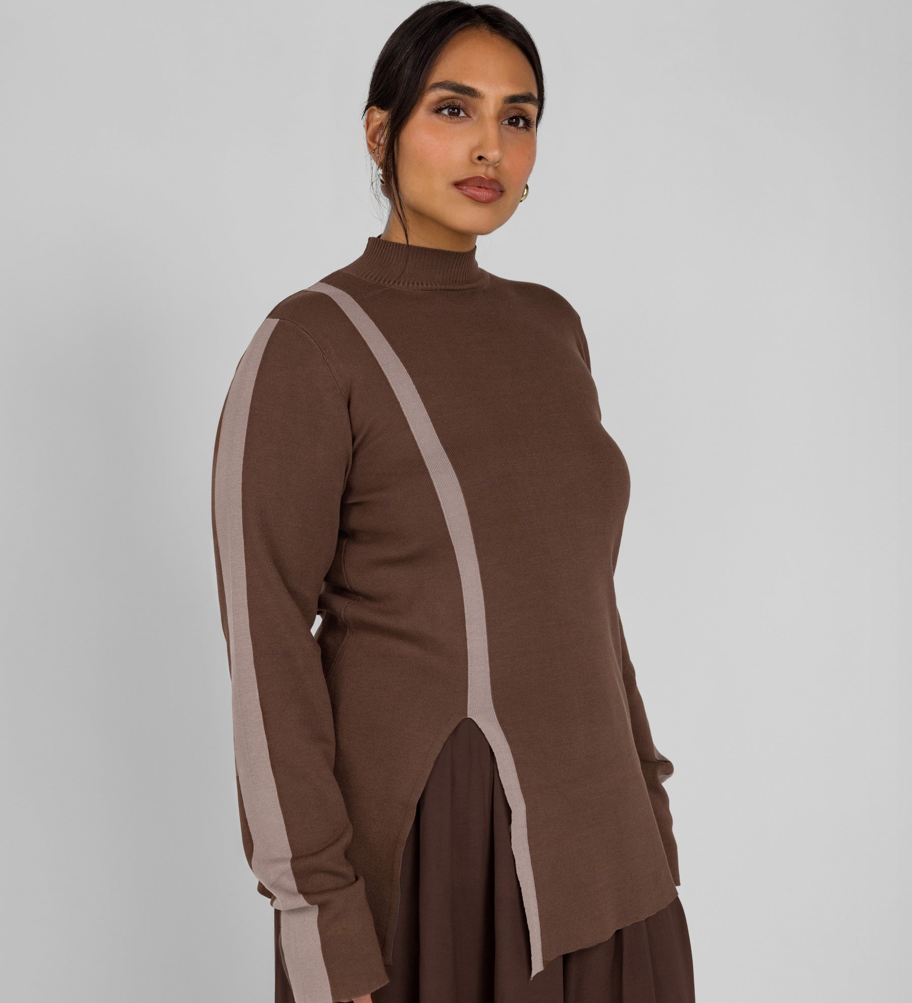 Woman wearing a brown outfit with a high collar and side slits on a plain background