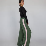 Woman wearing green pants with pink stripes and a black top on a gray background