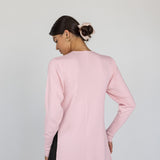 Woman wearing a light pink top over a black outfit on a plain background