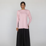 Person wearing a pink knit top and black pants on a white background