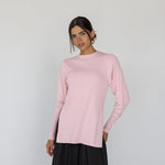 Woman wearing a light pink long-sleeve top and black pants on a white background