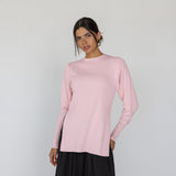 Woman wearing a light pink long-sleeve top and black pants on a white background