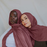 Two models wearing a rosey pink hijab, with one model partially behind the other, set against a neutral background.