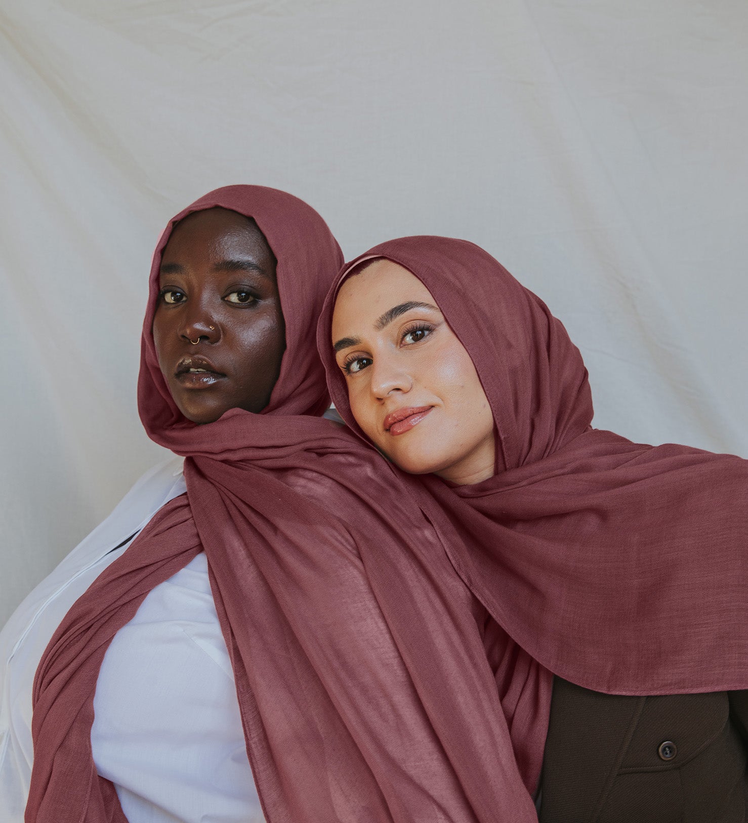Two models wearing a rosey pink hijab, with one model partially behind the other, set against a neutral background.