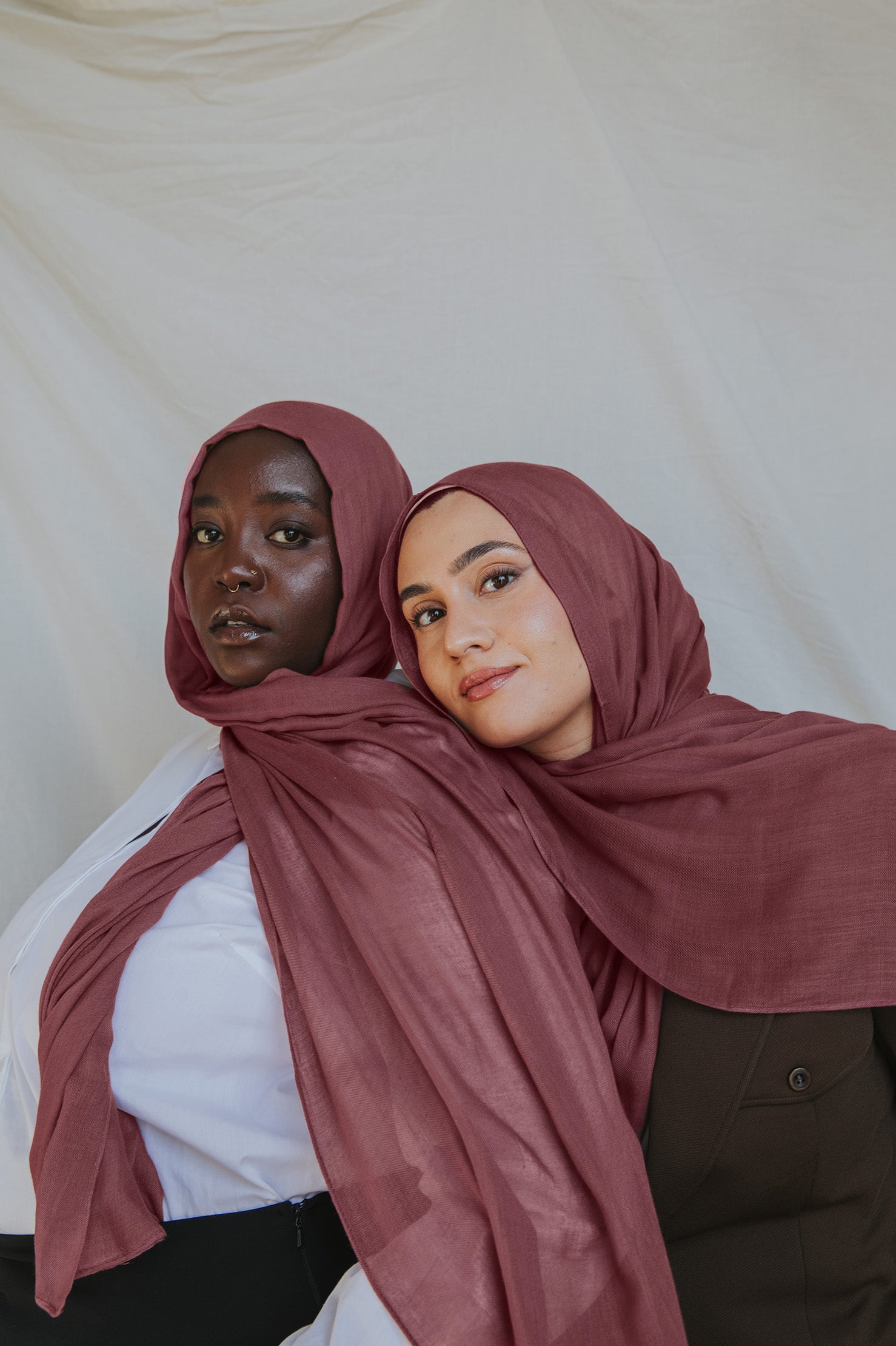 Two models wearing a rosey pink hijab, with one model partially behind the other, set against a neutral background.