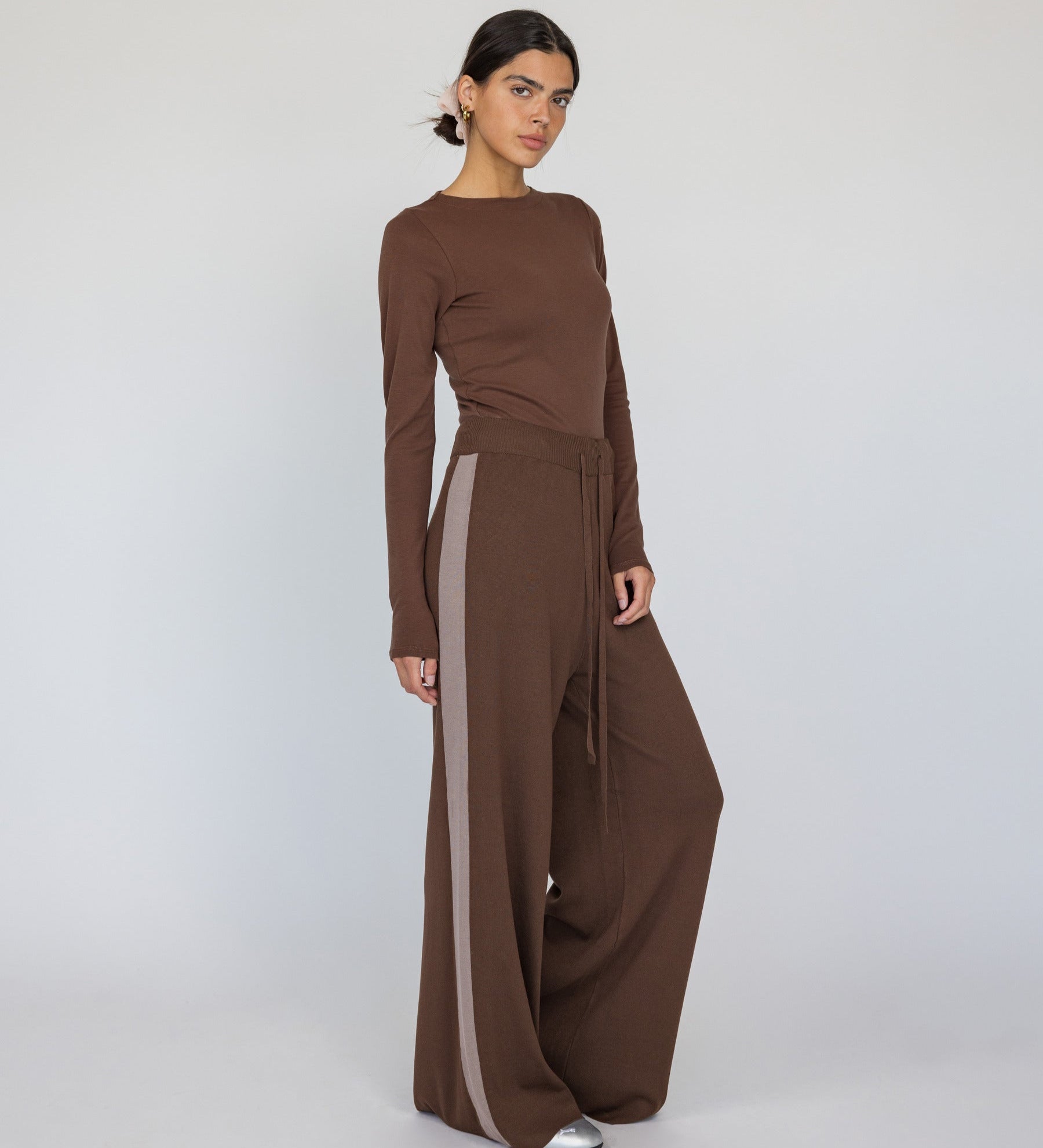Woman wearing a brown long-sleeve top and wide-leg pants with a white background