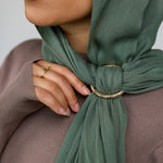 Person wearing a green hijab with a gold hijab hoop, against a neutral background.