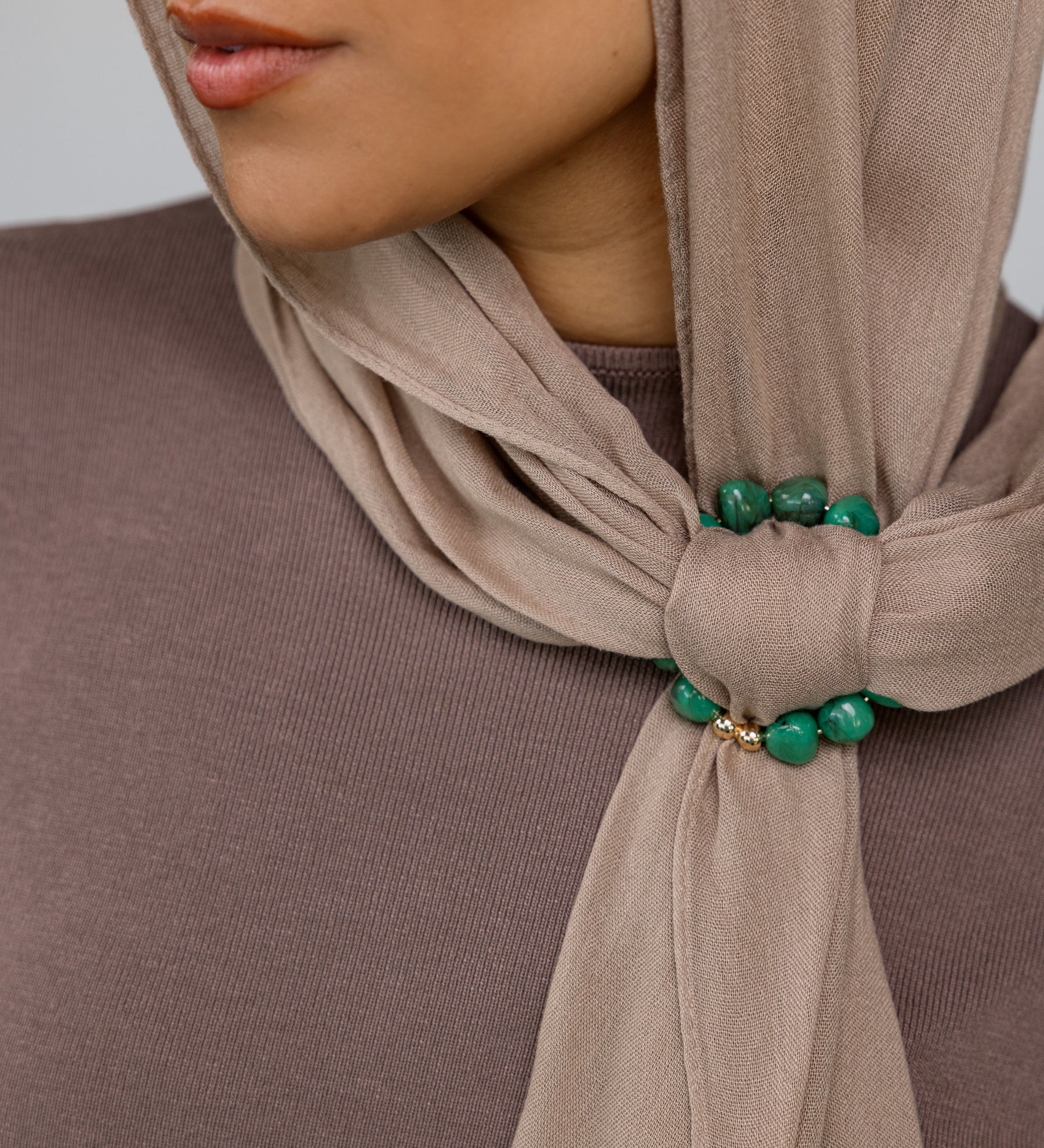Close-up of a beige hijab with emerald green hoop on a neutral background.