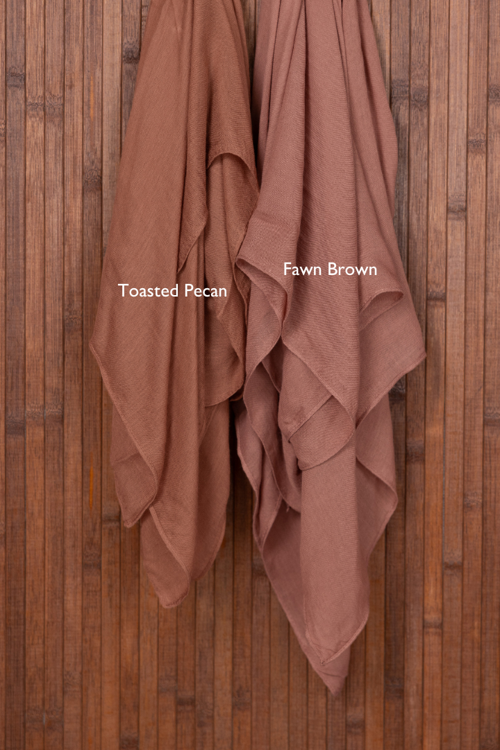 Color comparison of two brown hijabs draped over a wooden surface with color swatches labeled 'Toasted Pecan' and 'Fawn Brown'.