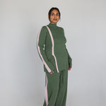 Person wearing a green outfit with pink accents on a plain background