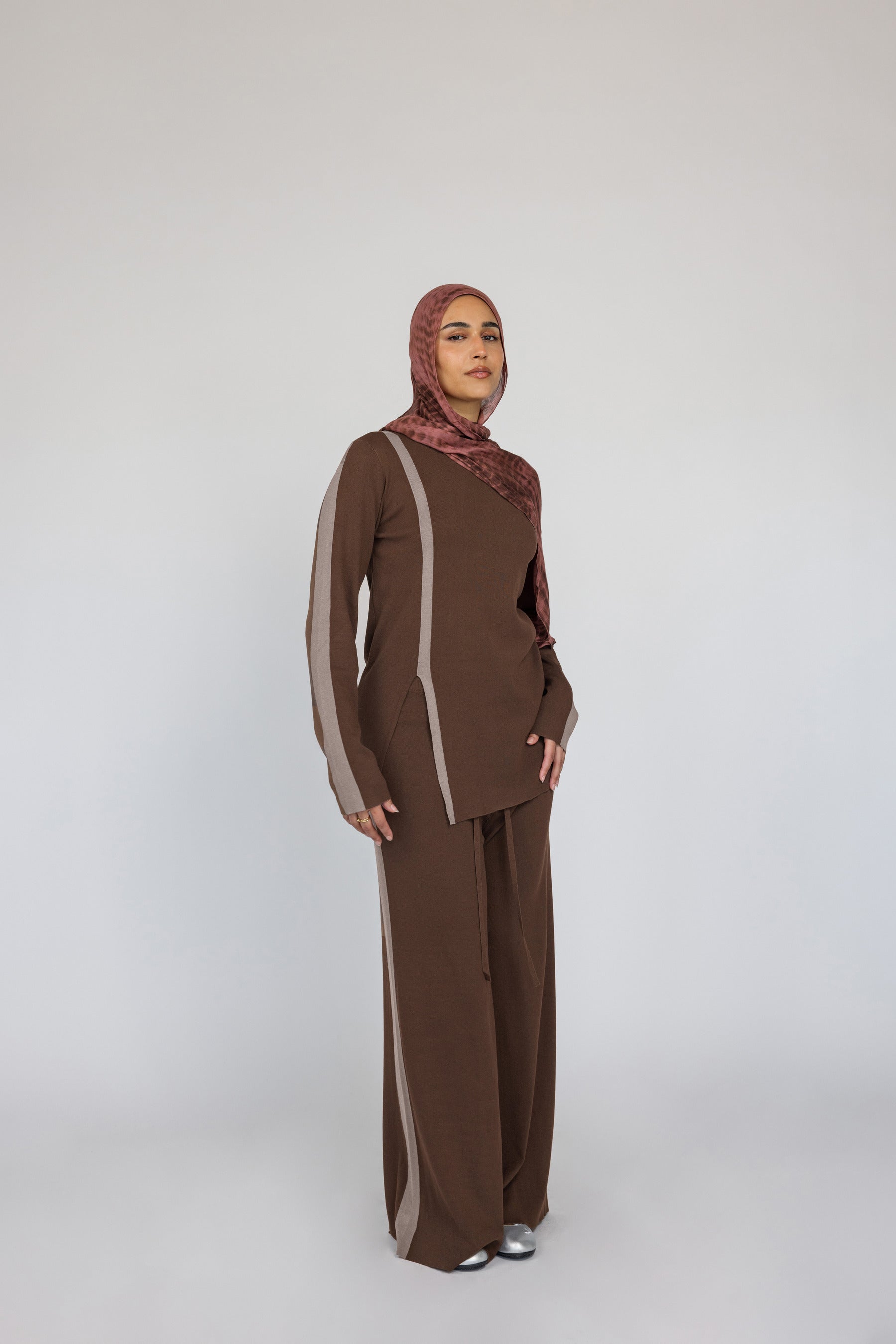 Woman wearing a brown striped matching outfit with a red clay ripple print hijab on a white background