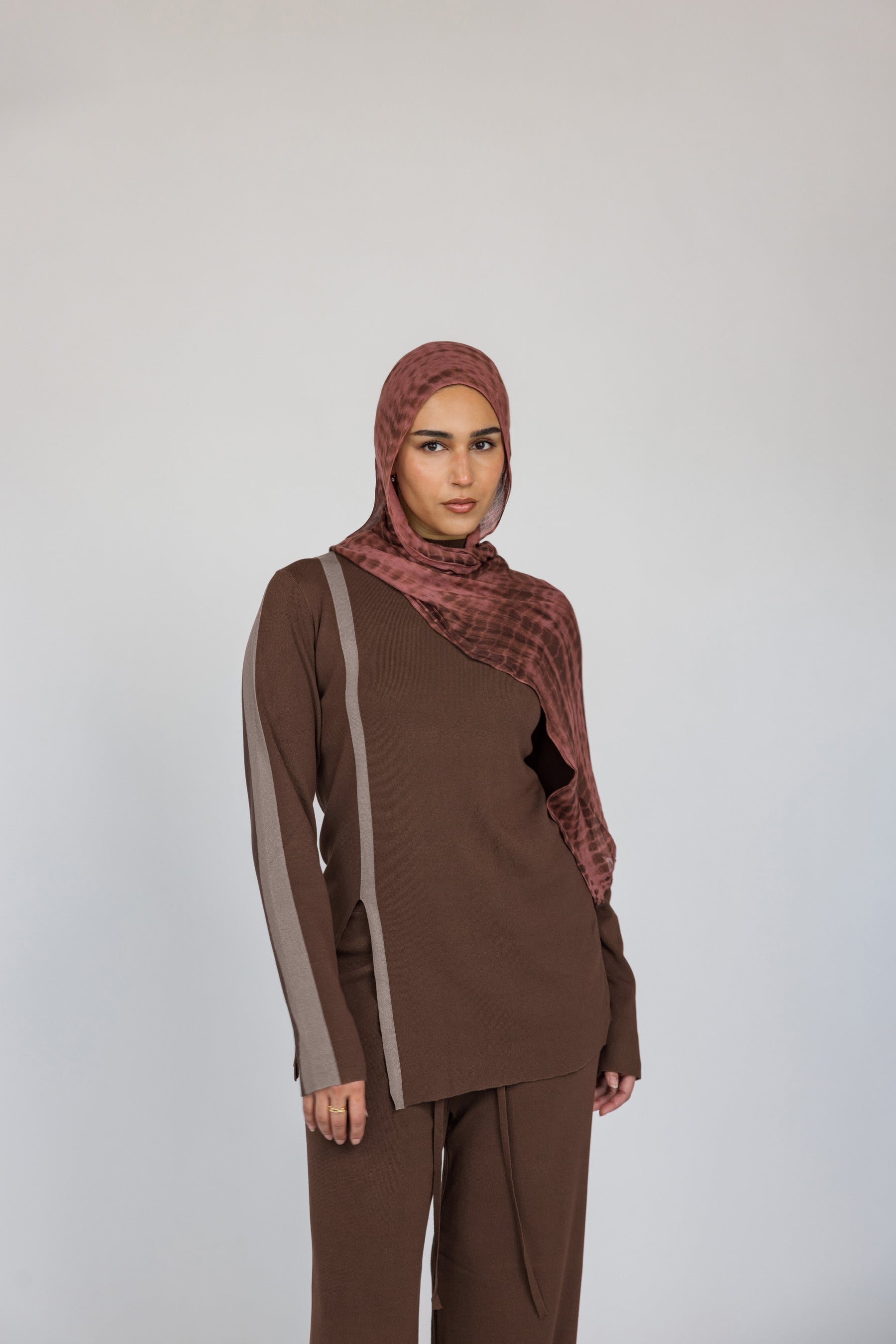 Model styled a brown outfit with a red clay ripple print hijab on a white background