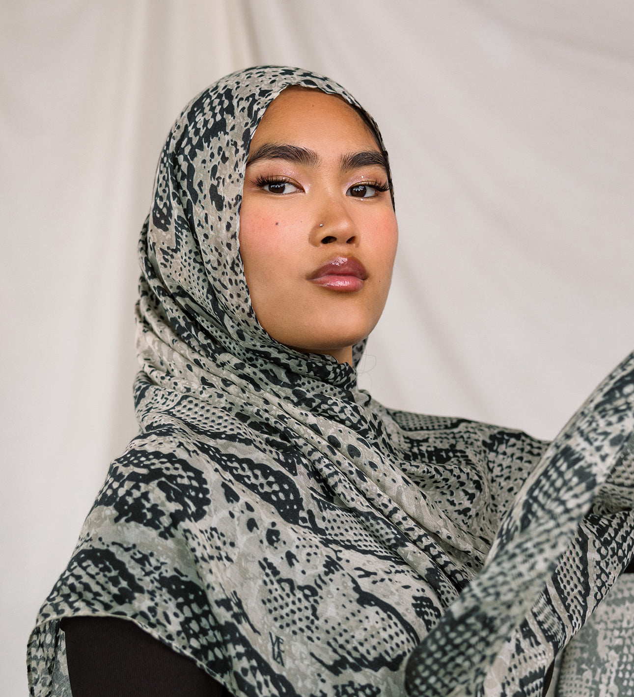 Close up shot of model wearing the Ink Cobra scarf by VELA, featuring a cool-toned, grey scale, snakeskin pattern on the scarf.