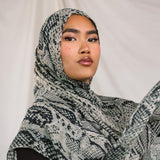 Close up shot of model wearing the Ink Cobra scarf by VELA, featuring a cool-toned, grey scale, snakeskin pattern on the scarf.