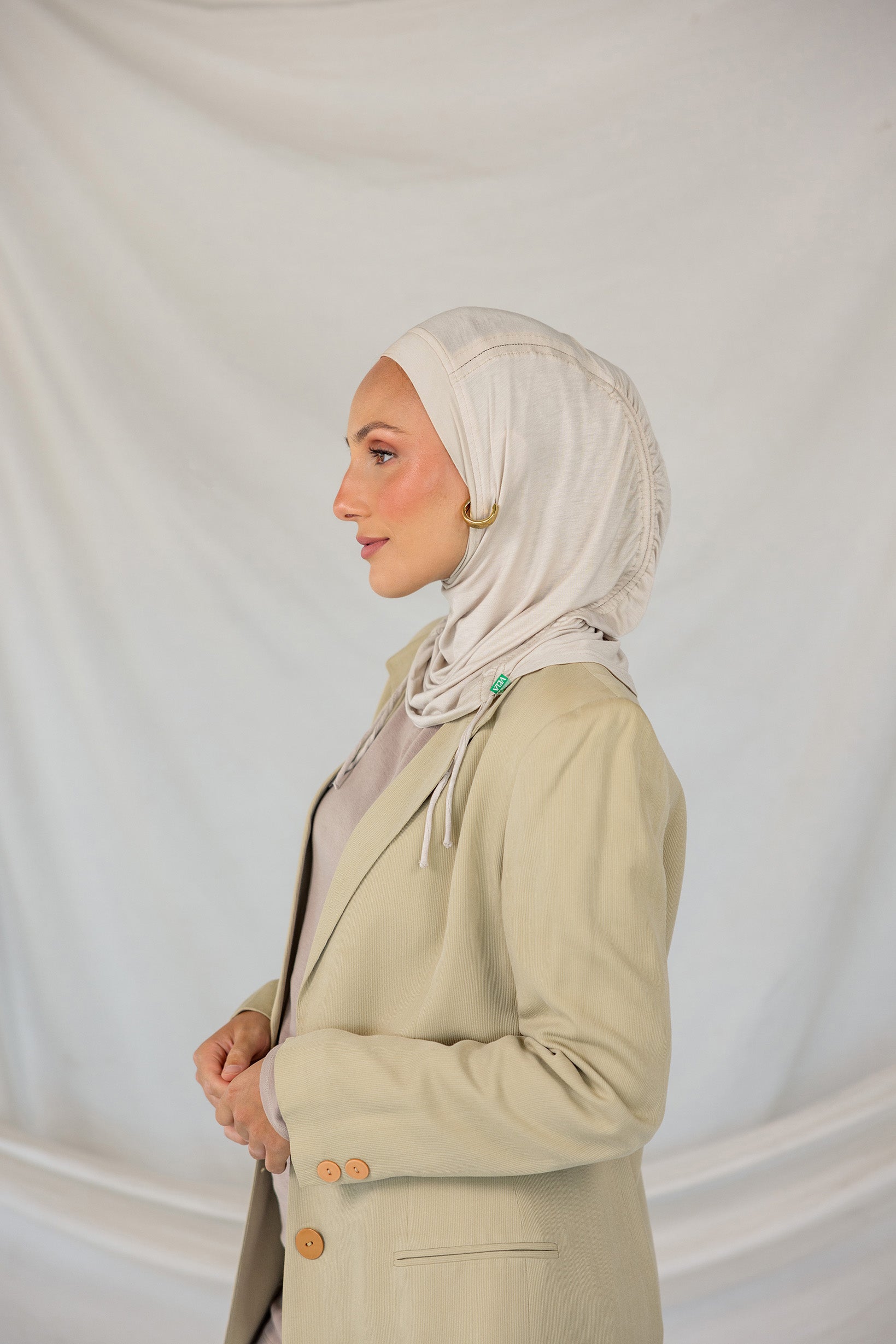 Model wearing Ashwood Ruching Lite fabric draped against white backdrop, revealing beige-ash tone and ruched design.