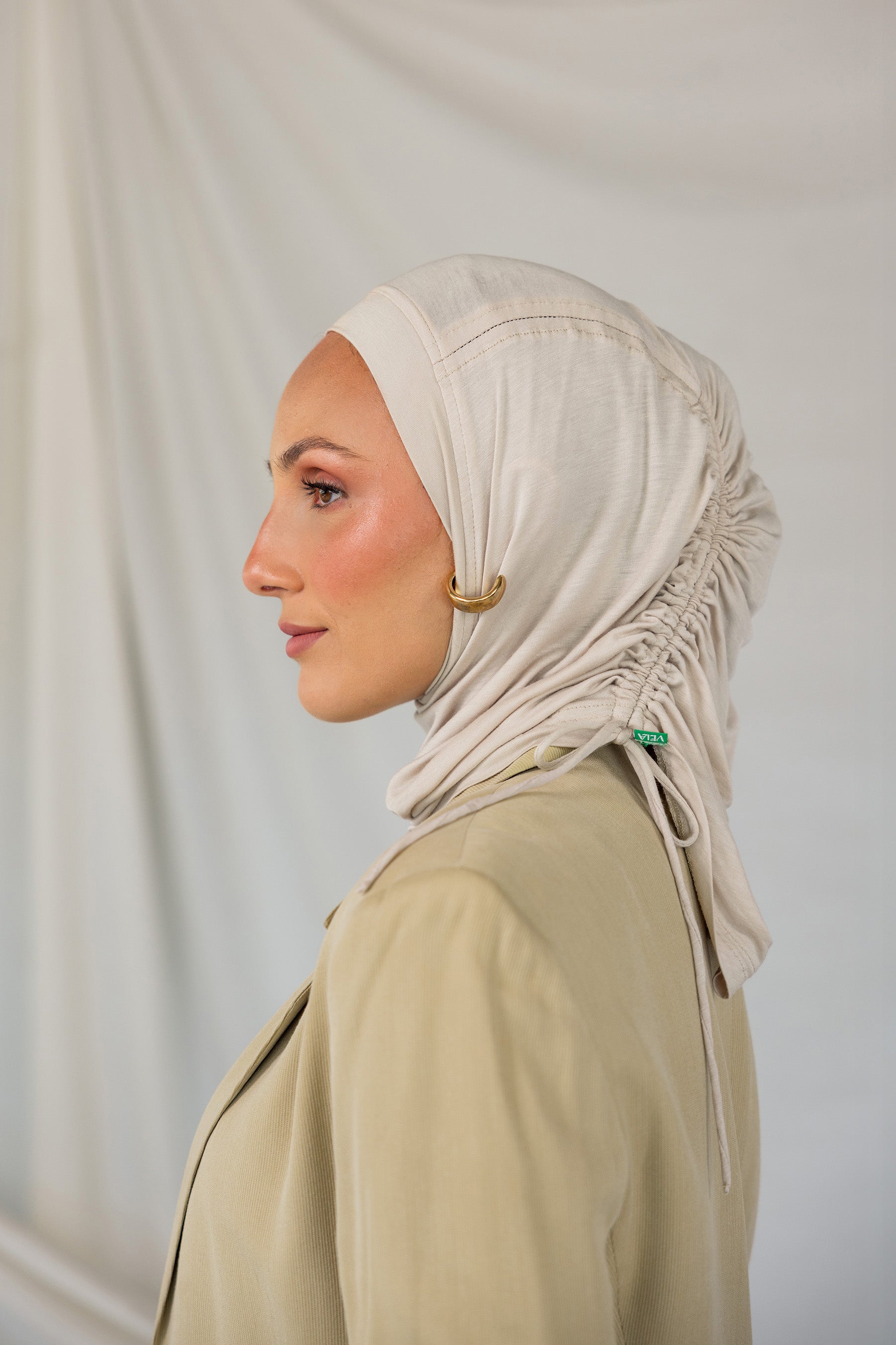 Woman wearing a beige ruching hijab and beige top against a plain background.