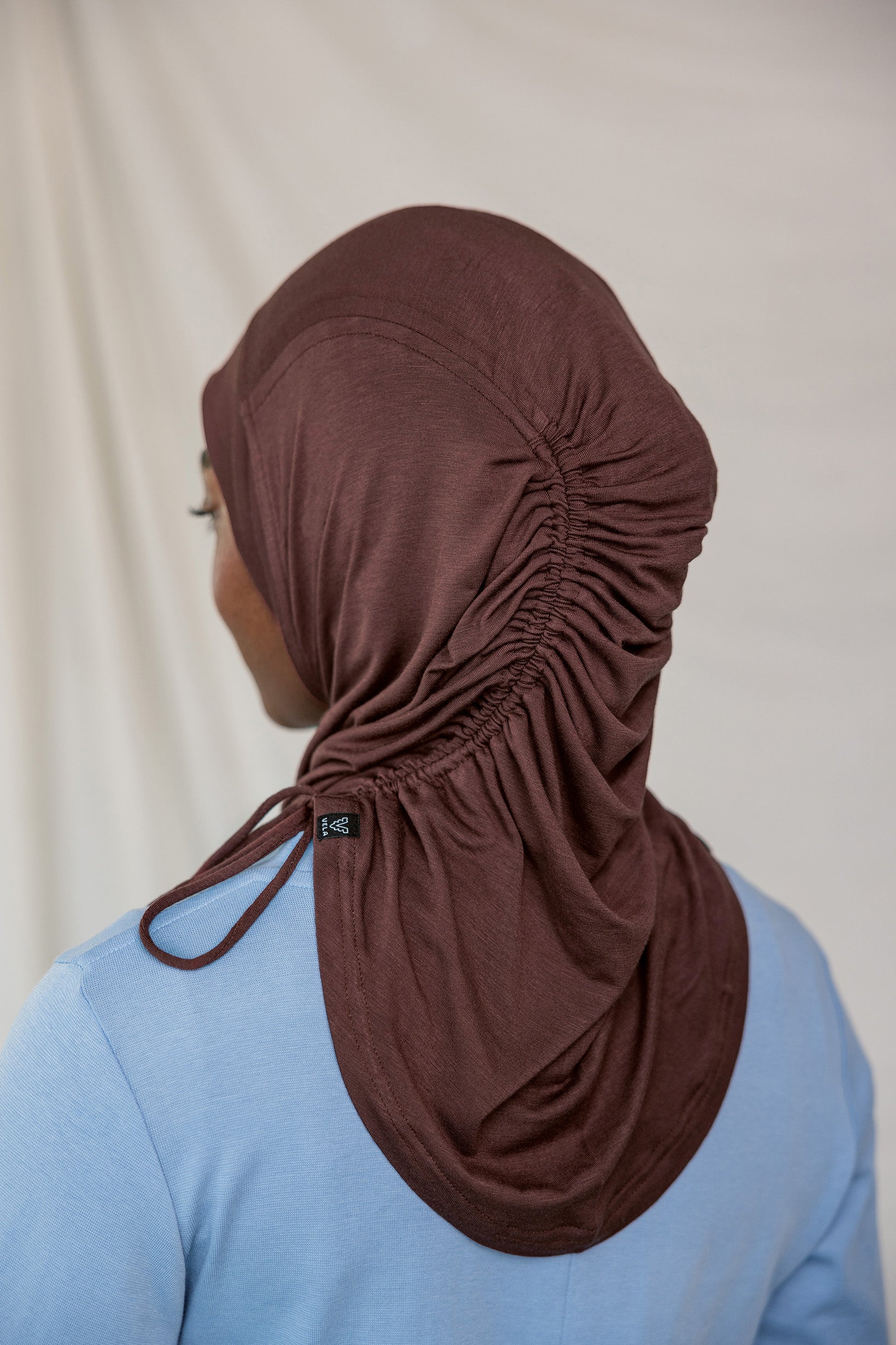 Model wearing a brown coffee hijab with a blue shirt against a beige background to show ruching back detail.