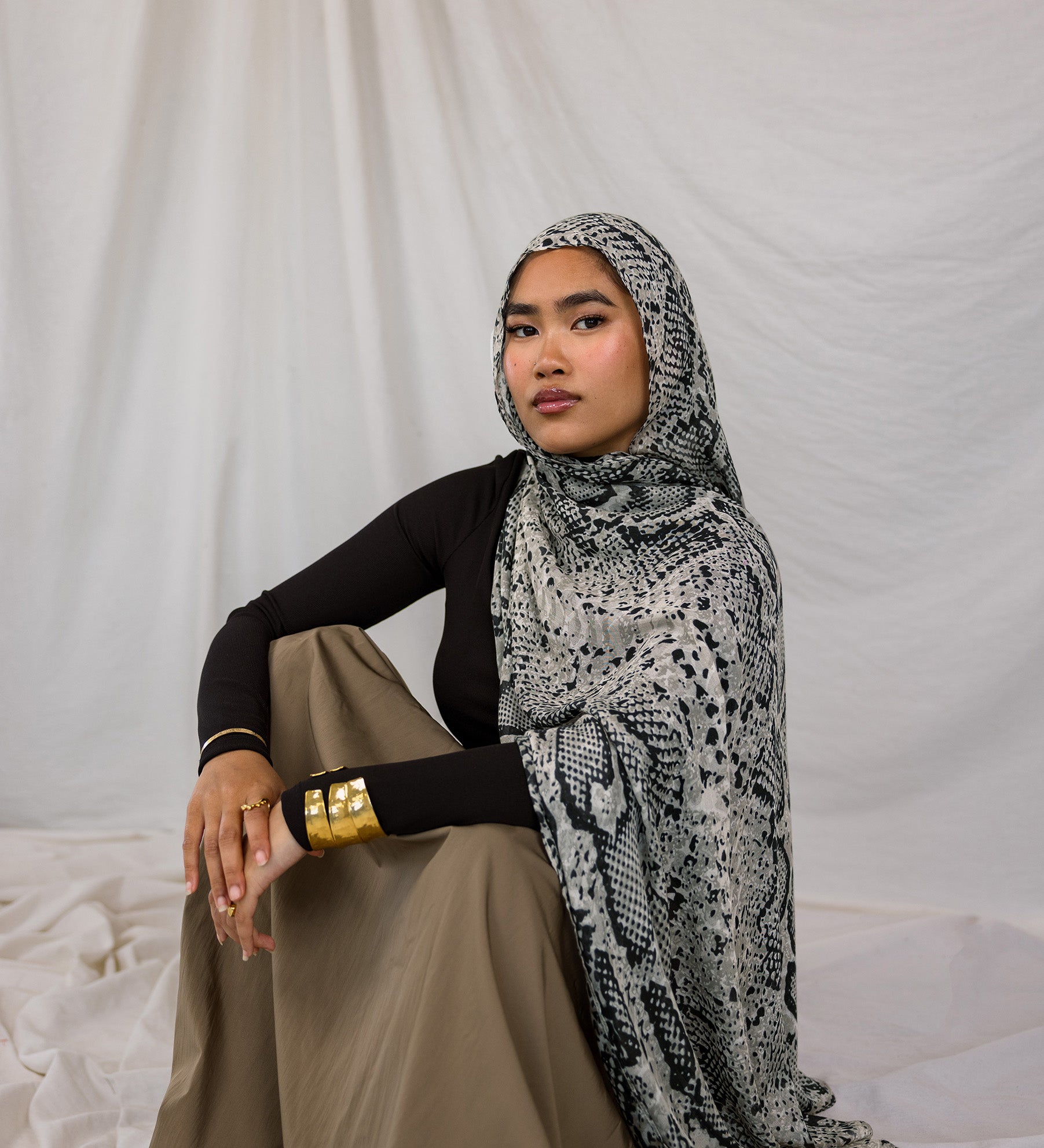 Model shown sitting down and posing in Ink Cobra, a grey-toned snakeskin print scarf by VELA.
