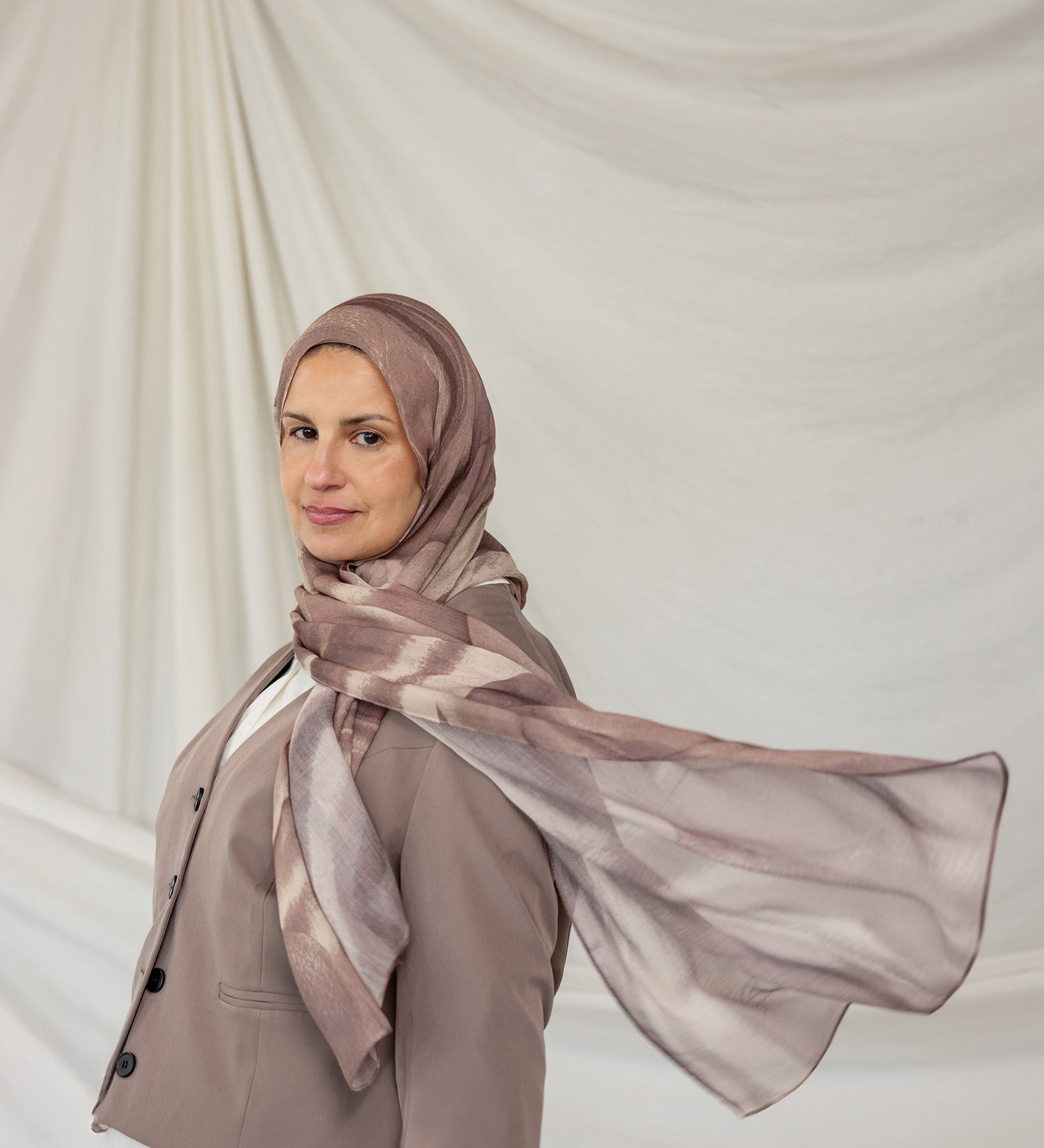 Woman wearing a brown gray sediment printed hijab and coat against a plain background