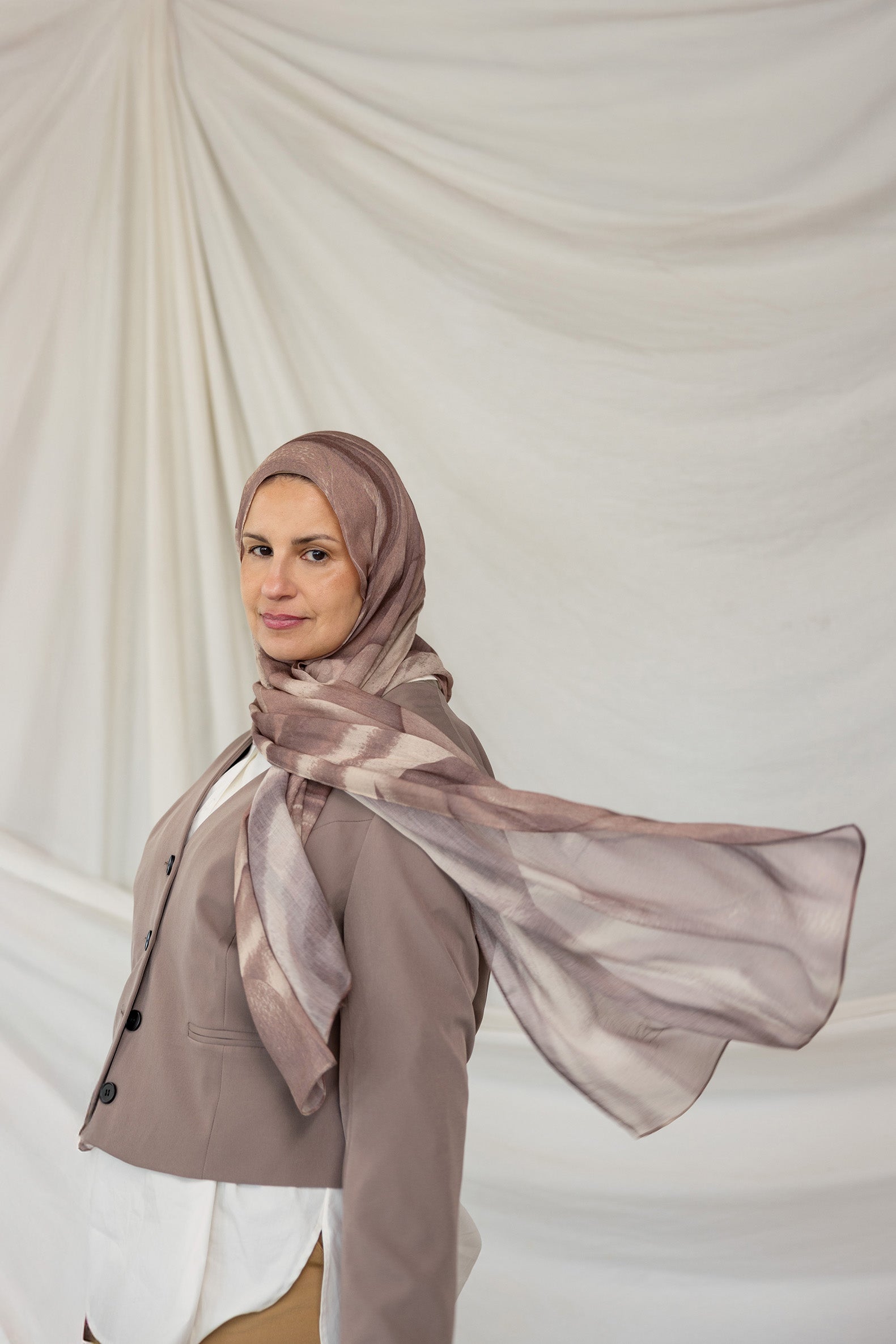 Woman wearing a brown gray sediment printed hijab and coat against a plain background