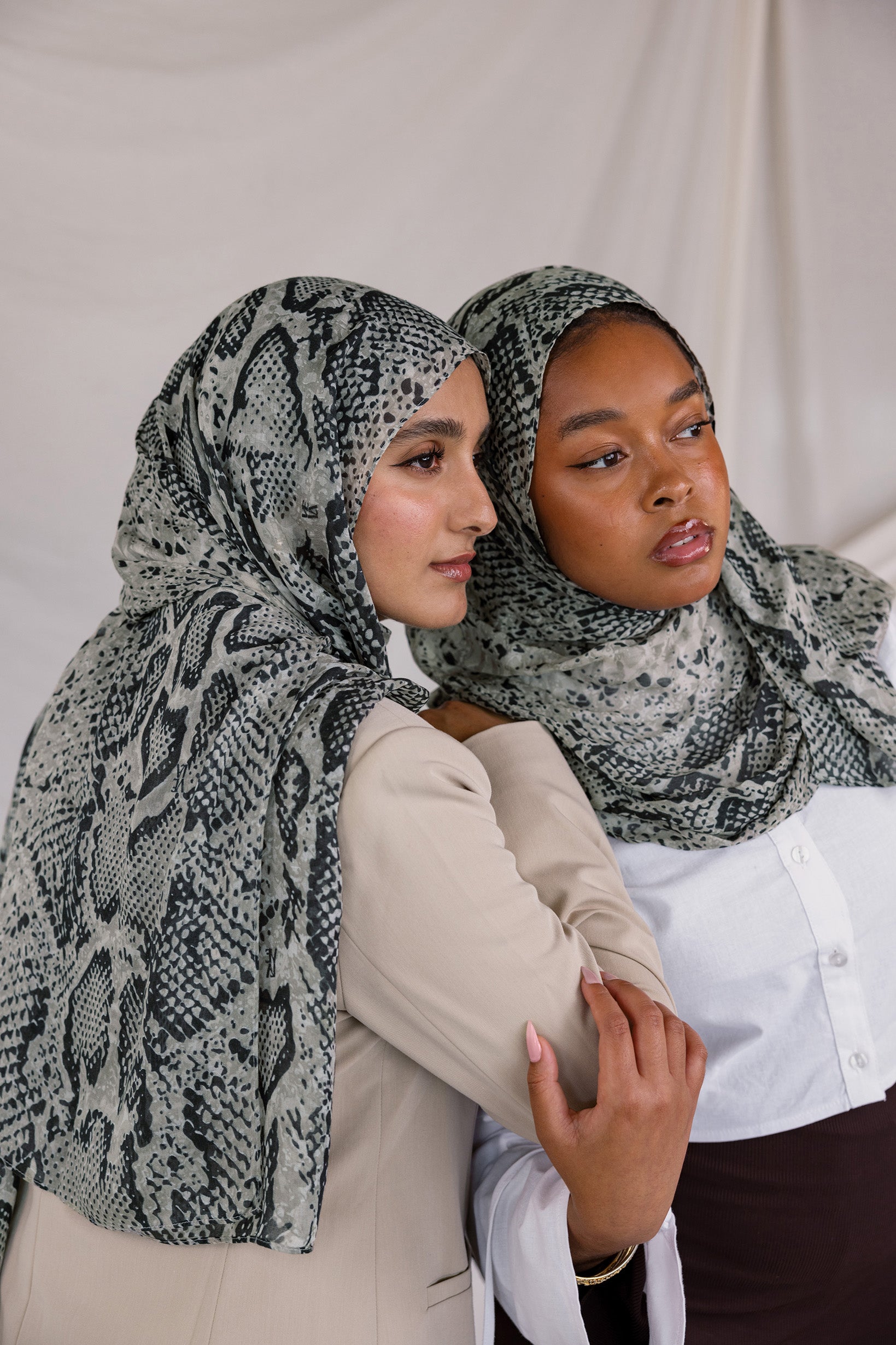Two models posing together showing their Ink Cobra VELA hijab. This hijab features greys, blacks, and whites in a snakeskin-like pattern.