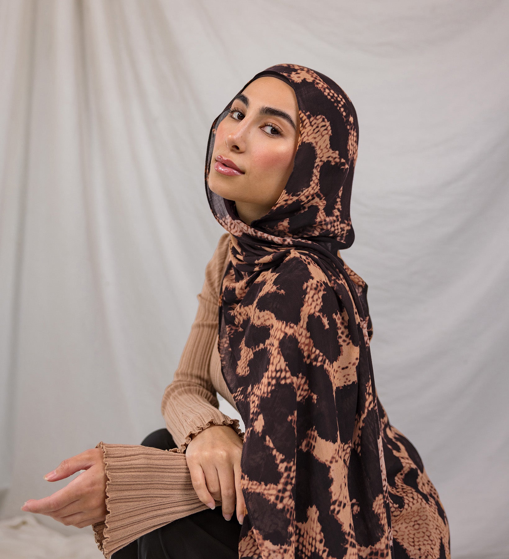 Model wearing a peach and tan based scarf with dark brown spots, called the Wild Savanna print.