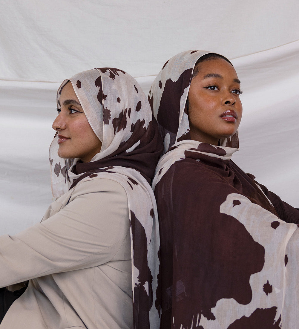 Two models shown posing back to back, both wearing the Prairie Hide print that is a cow/western inspired print with a cream base and brown splotches to mimic a hide.