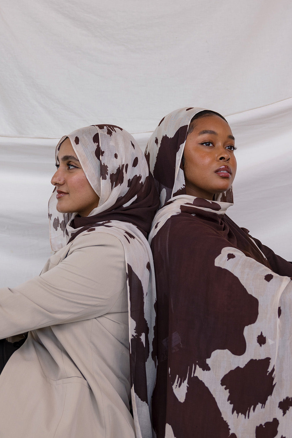 Two models shown posing back to back, both wearing the Prairie Hide print that is a cow/western inspired print with a cream base and brown splotches to mimic a hide.