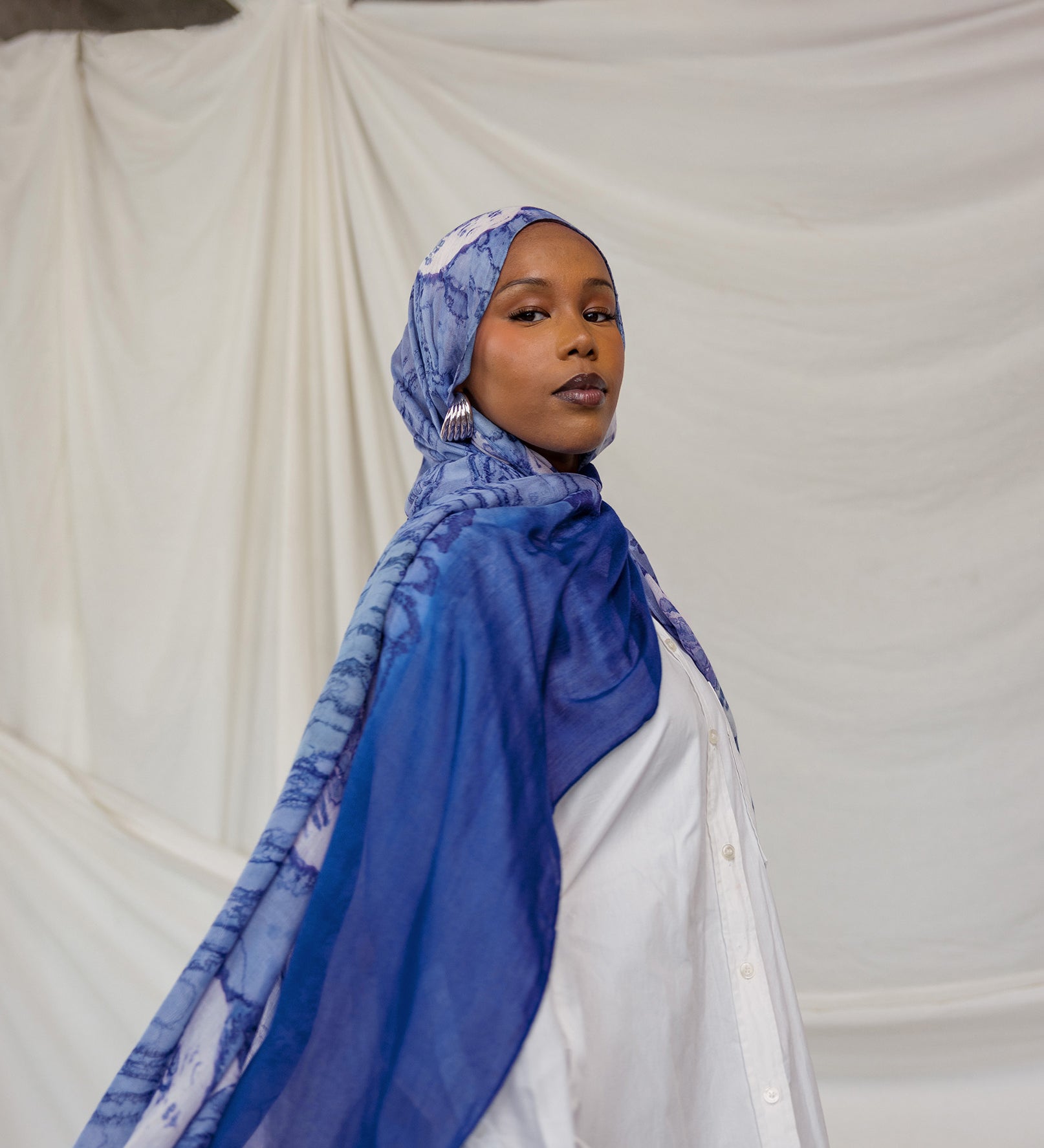 Woman wearing a royal blue and white shell printed headscarf against a plain background