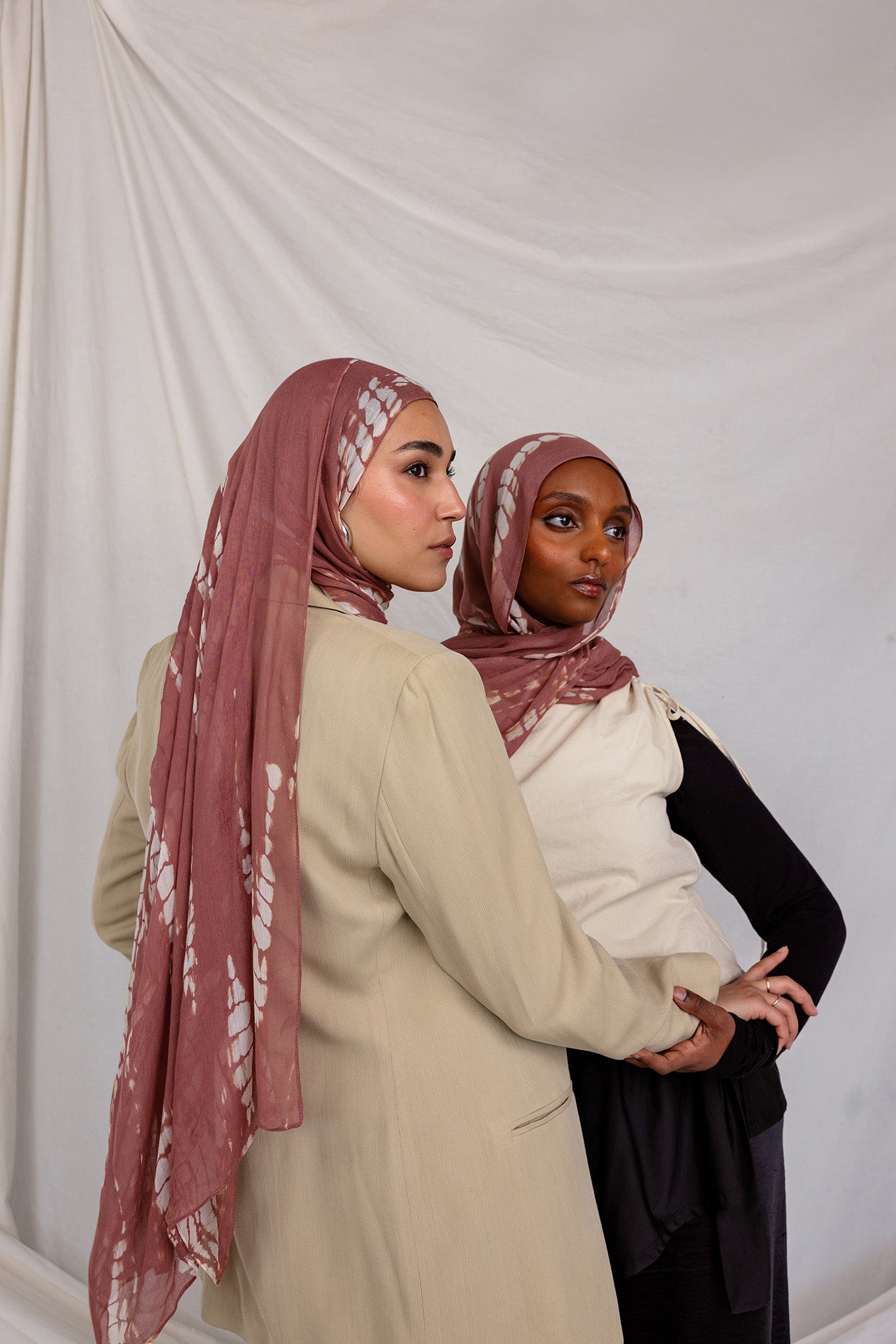 Two women wearing matching pink printed ripple pattern hijabs against a white background