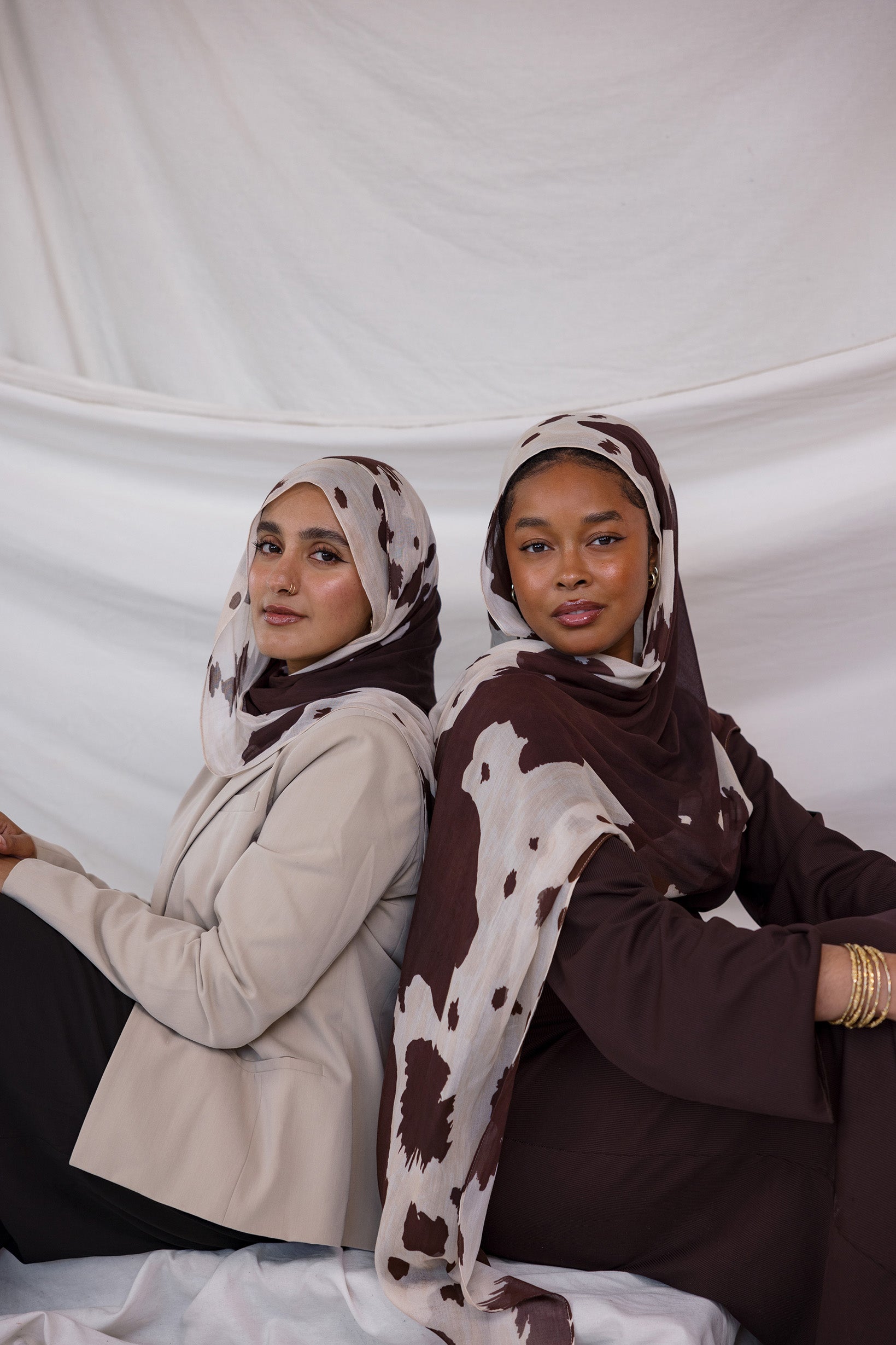 Two models shown styled in two different ways, both wearing the cream and chocolate toned print, Prairie Hide, which has splotches like a cow hide.