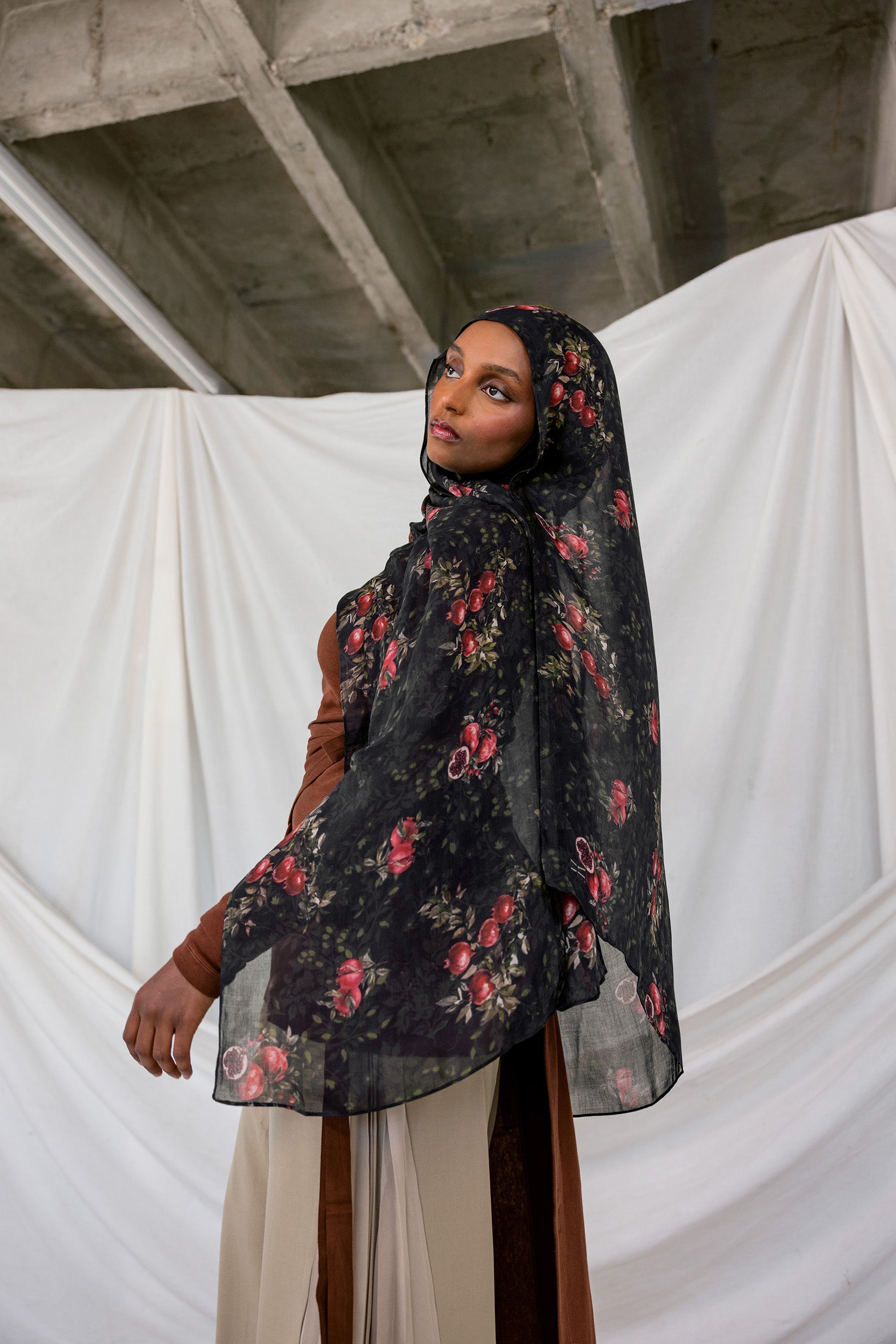 Woman wearing a black pomegranate hijab against a white curtain and concrete wall background