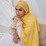 Woman wearing a bright yellow hijab laying on a white box.