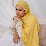 Woman wearing a bright yellow hijab laying on a white box.