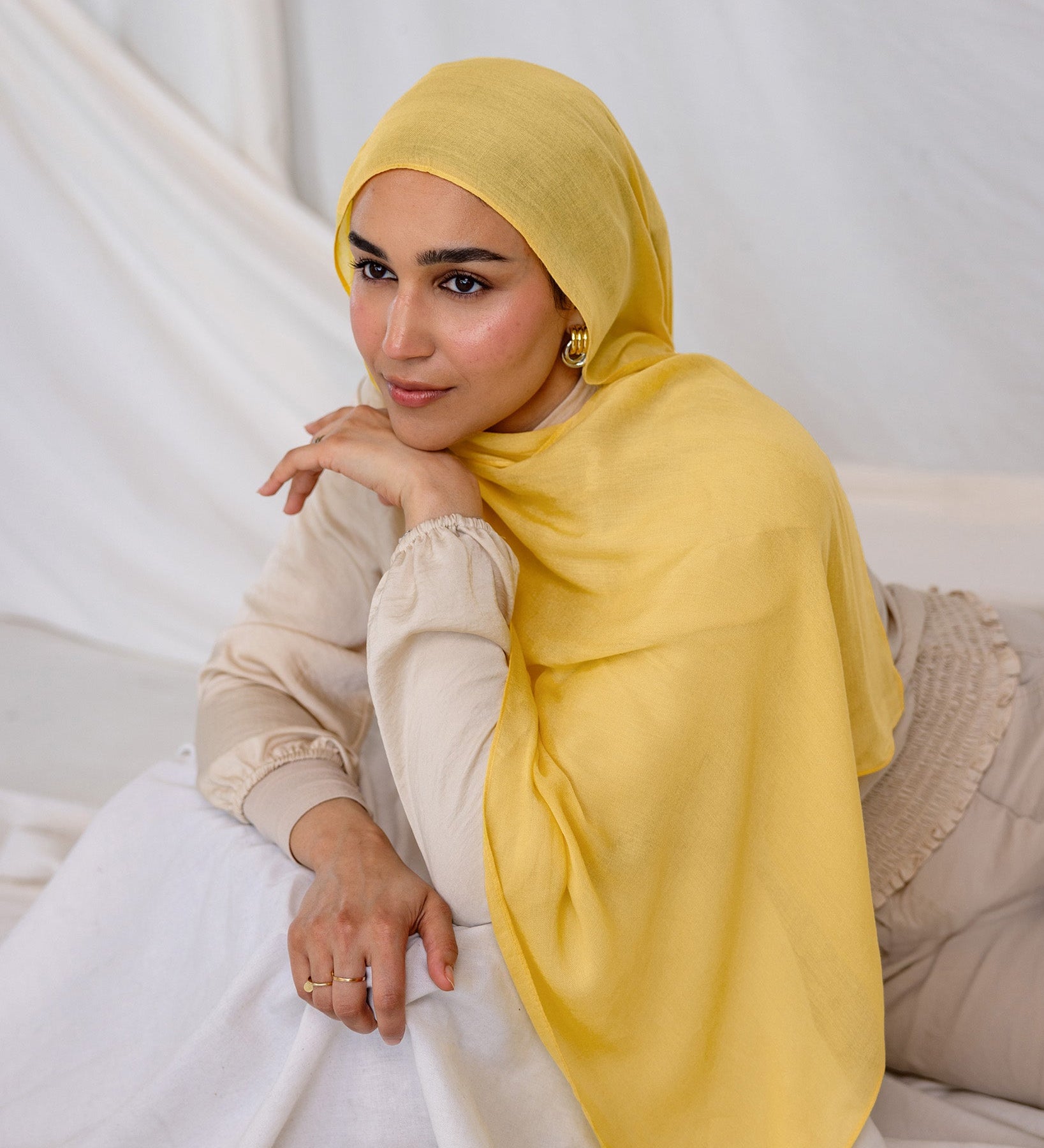 Woman wearing a bright yellow hijab laying on a white box.