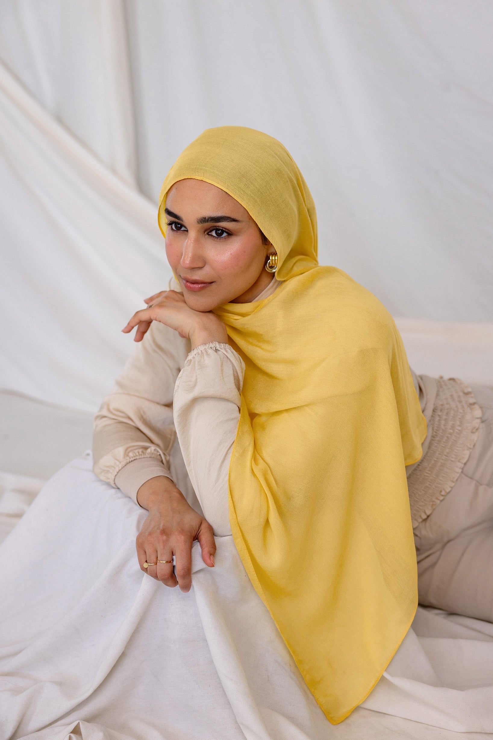 Woman wearing a bright yellow hijab laying on a white box.
