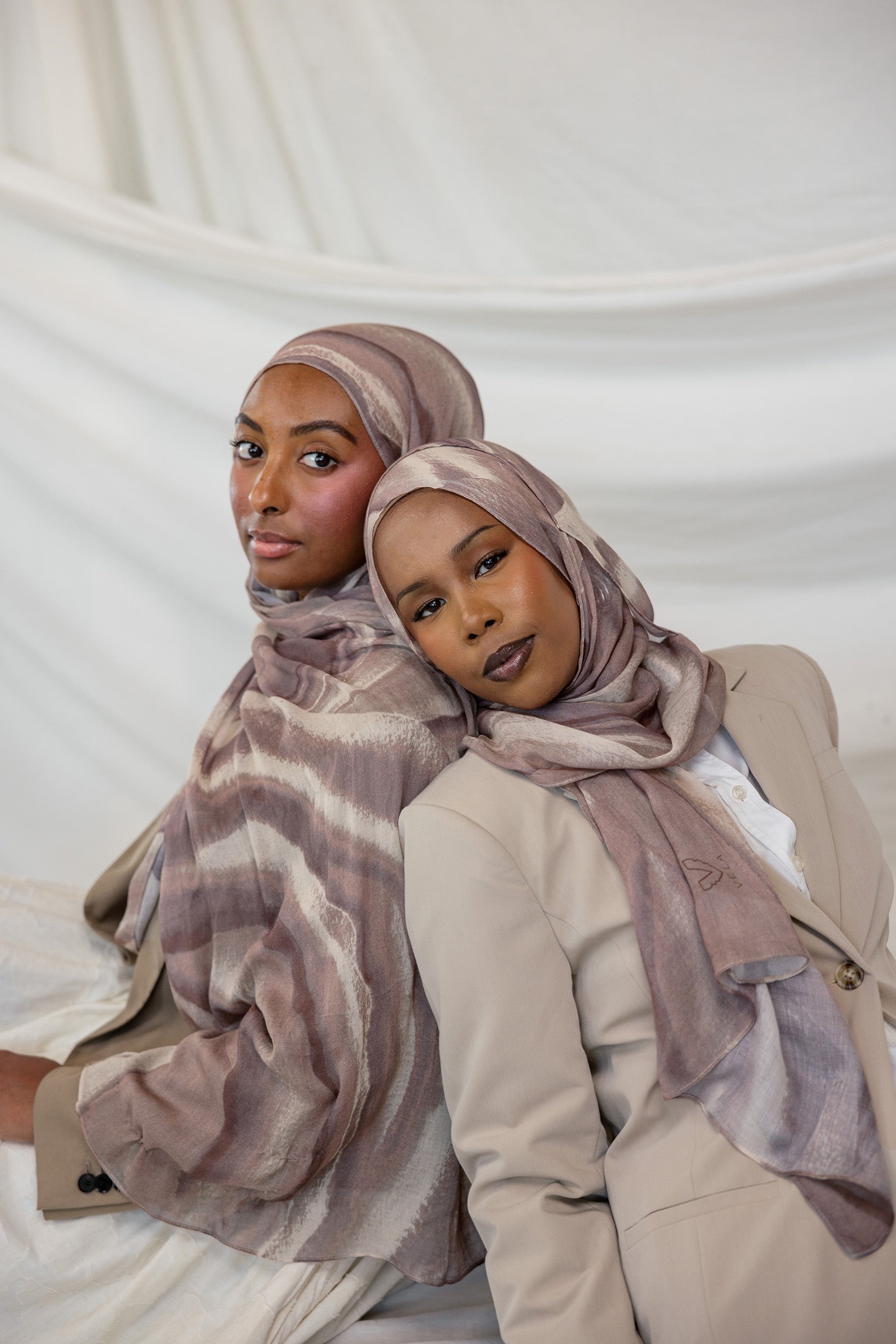 Two women wearing brown sediment printed hijabs against a white background
