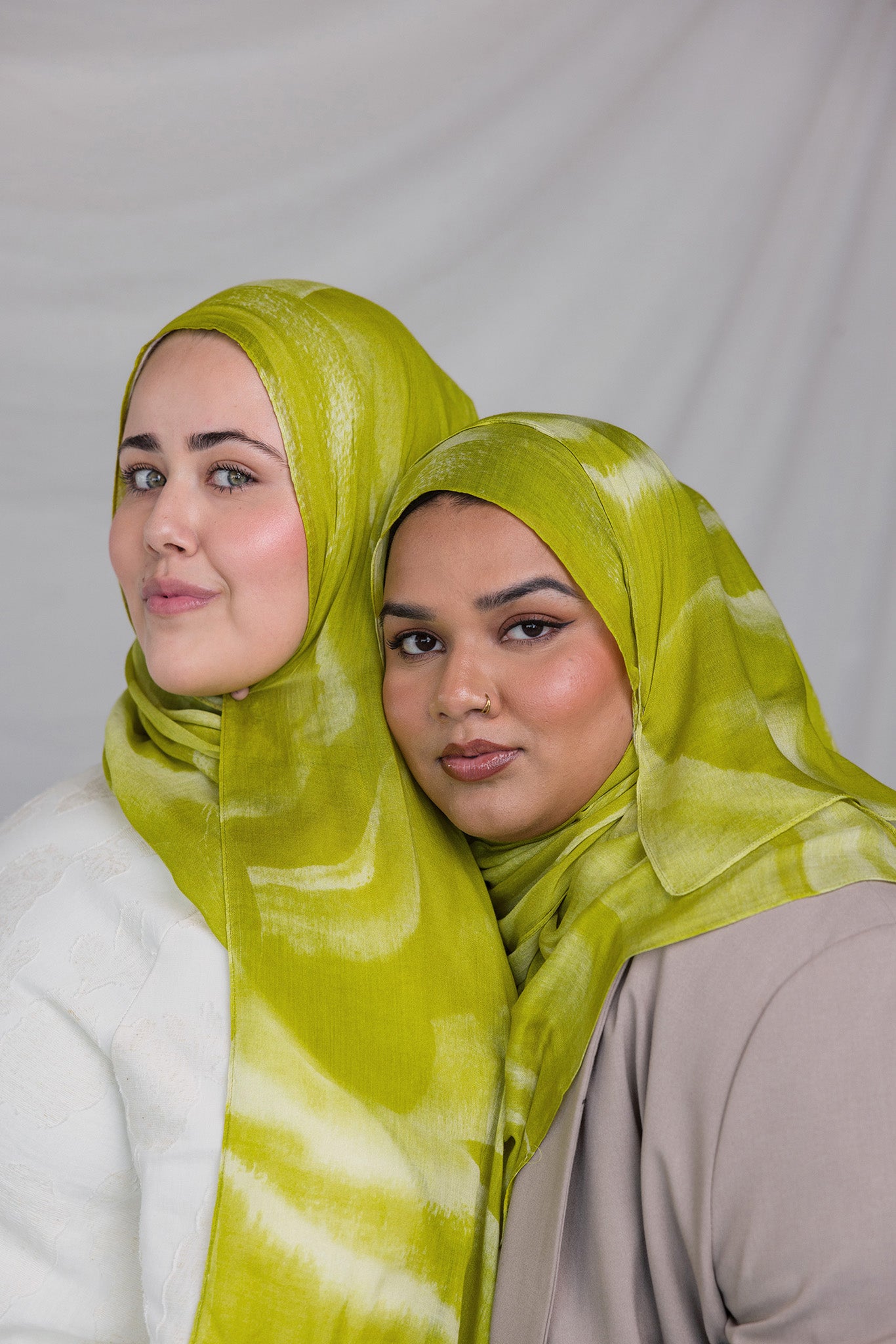 Two women wearing lime green sediment printed headscarves against a plain background
