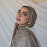 A woman wearing a truffle mushroom colored scarf, with a neutral background.