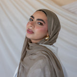 A woman wearing a truffle mushroom colored scarf, with a neutral background.