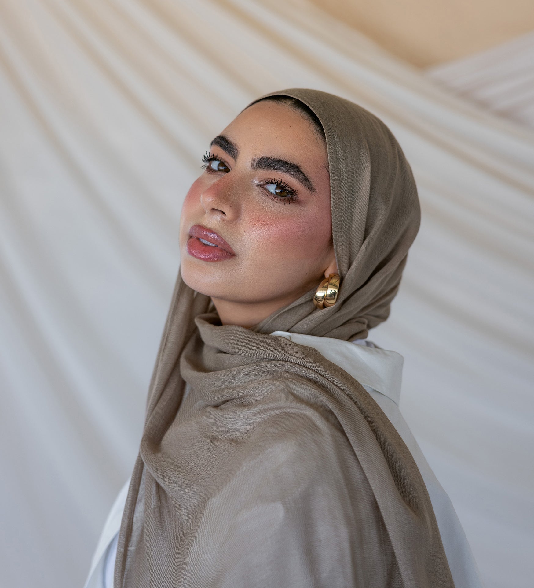 A woman wearing a truffle mushroom colored scarf, with a neutral background.