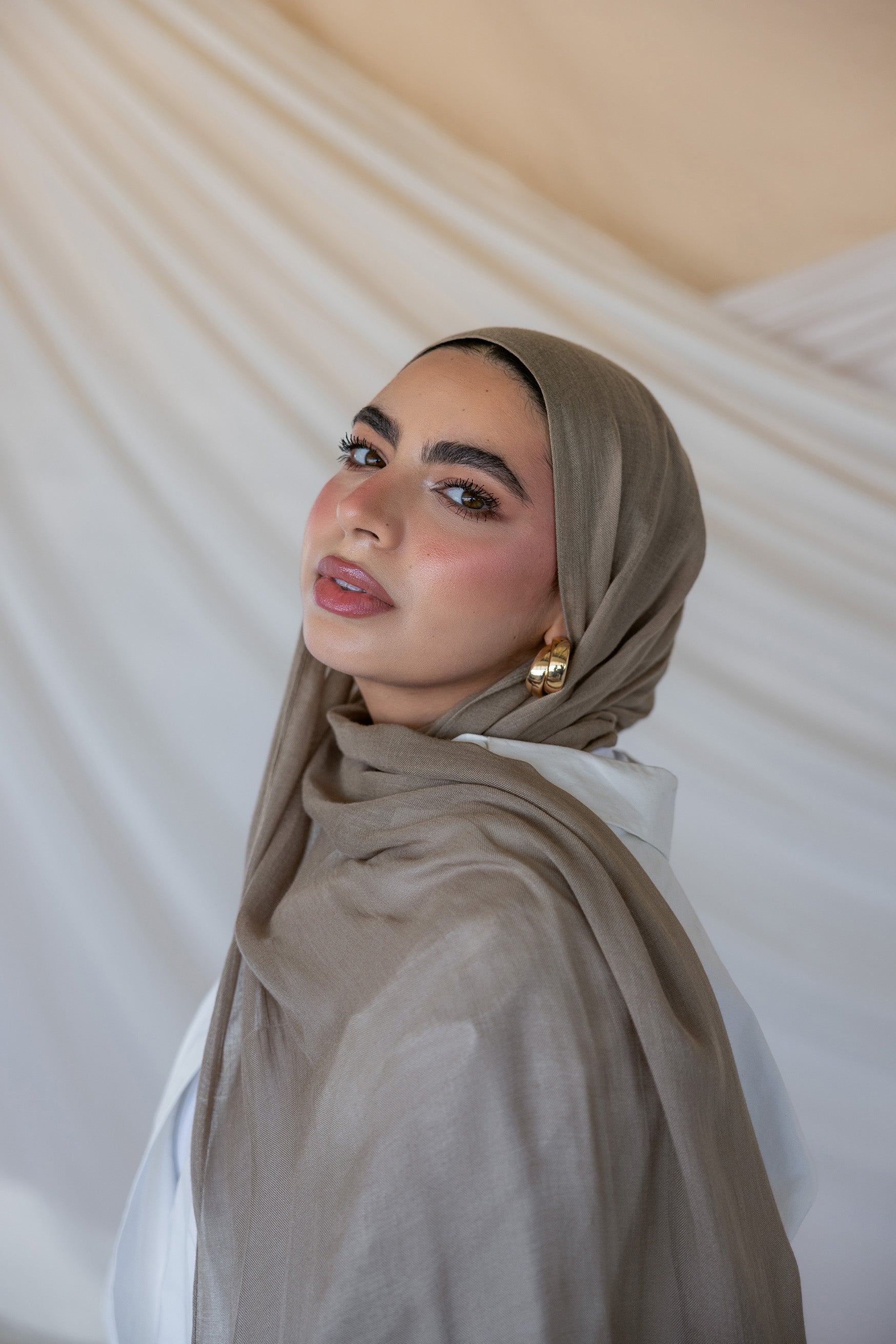 A woman wearing a truffle mushroom colored scarf, with a neutral background.