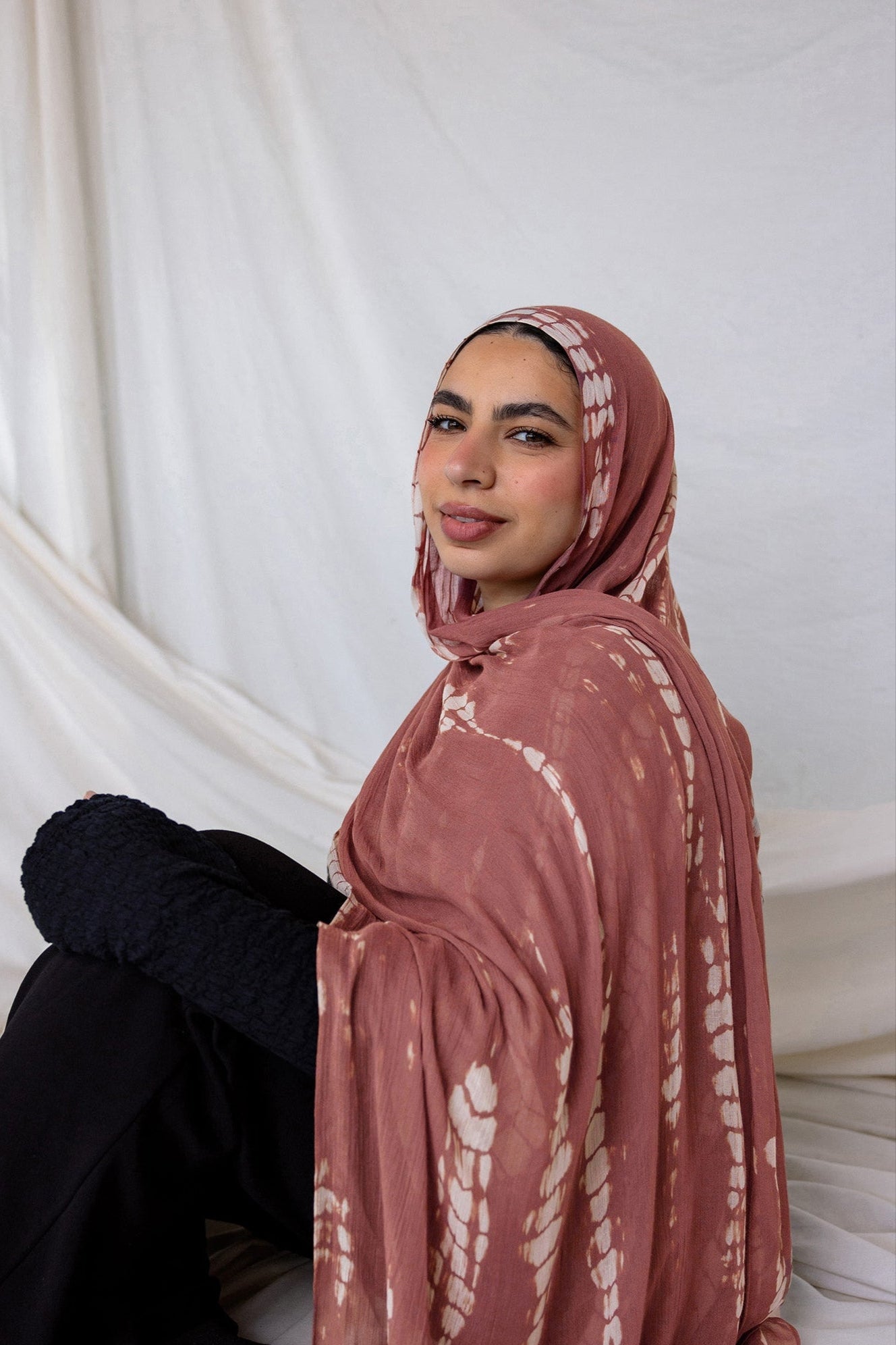 Woman wearing a pink hijab with white ripple patterns against a white curtain background