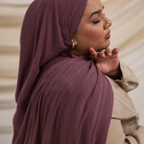 A person wearing a rose colored hijab, matching with a neutral outfit, in a soft lighting environment.